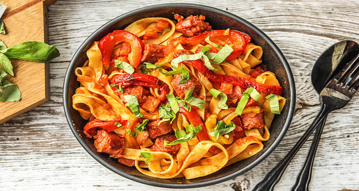 Fettucine aux chipolatas dans une sauce tomate piquante Avec des poivrons grillés, de la harissa et du basilic