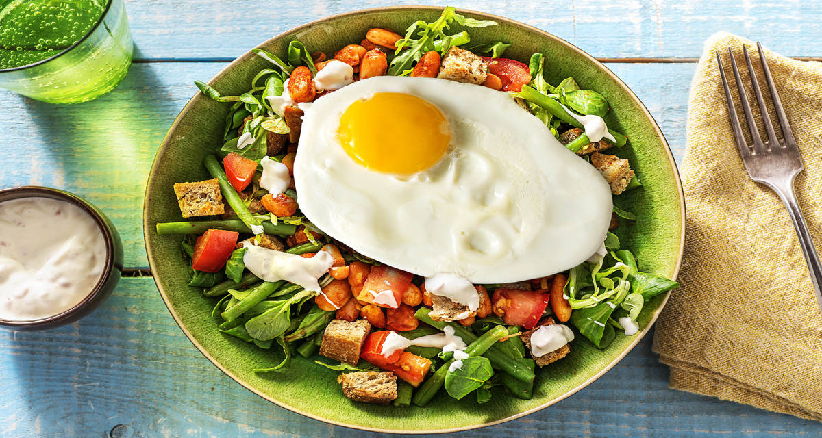 Salade de haricots, croûtons et œuf au plat Avec de la tomate et une vinaigrette onctueuse