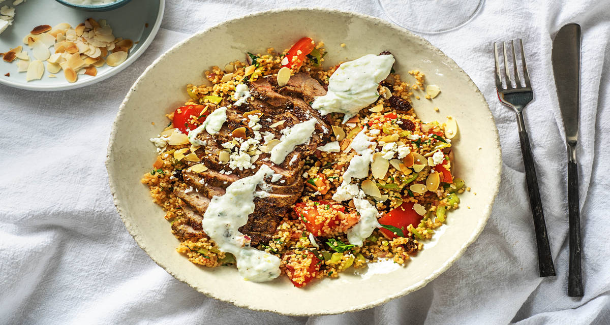 Échine de porc marinée au tzatziki Avec du couscous à la tomate, des raisins secs et de la feta