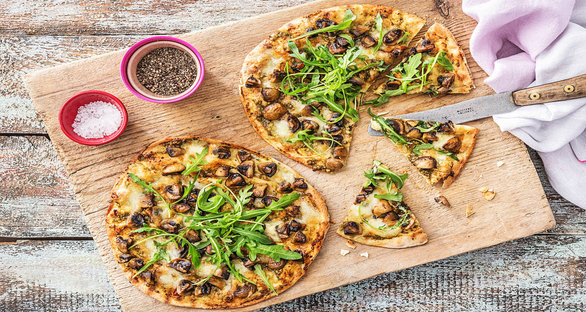 Pizza sur pain plat au pesto vert Avec de la mozzarella de bufflonne, des champignons et de la roquette