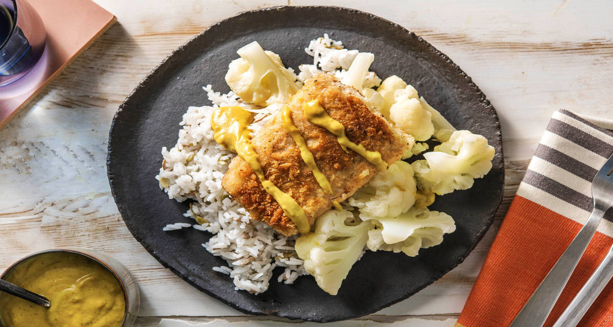 Filet de merlu pané accompagné de chou-fleur et d'une sauce au curry servi avec un riz aux graines