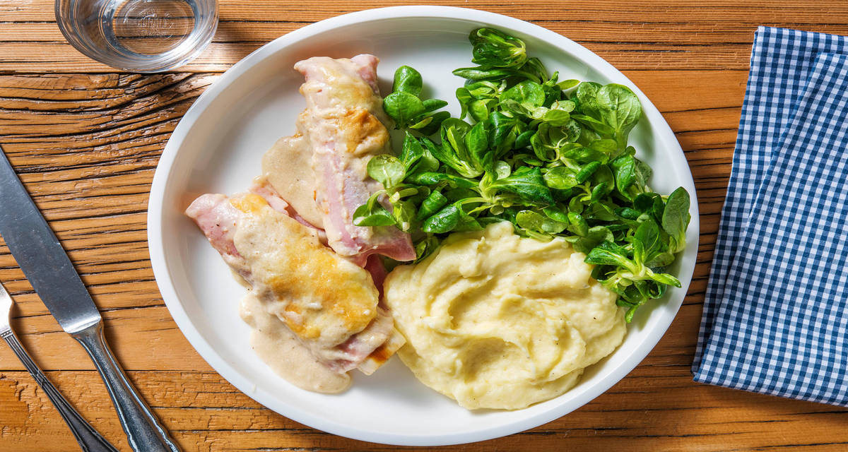 Rouleaux de poireau au jambon gratinés et sauce au fromage servis avec une purée de pommes de terre et une salade de mâche