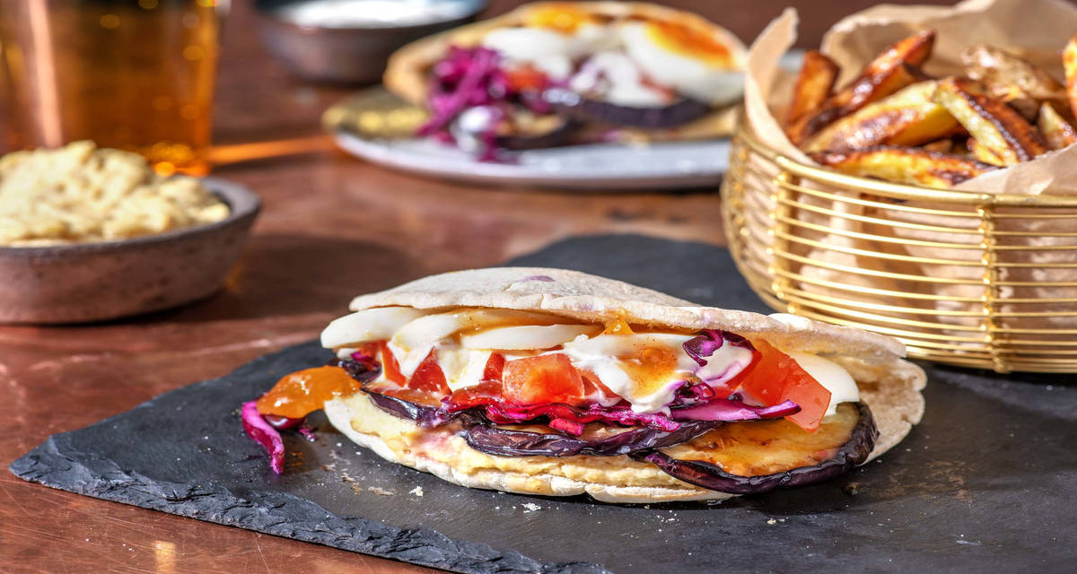 Sabich farci aux aubergines sautées et aux oeufs durs servi avec des frites maison et de l'houmous