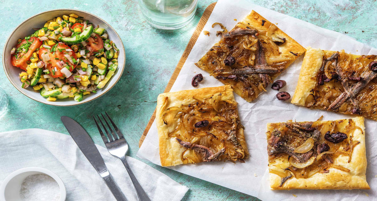 Tarte pissaladière feuilletée avec une salade de tomates, concombre, maïs et ciboulette