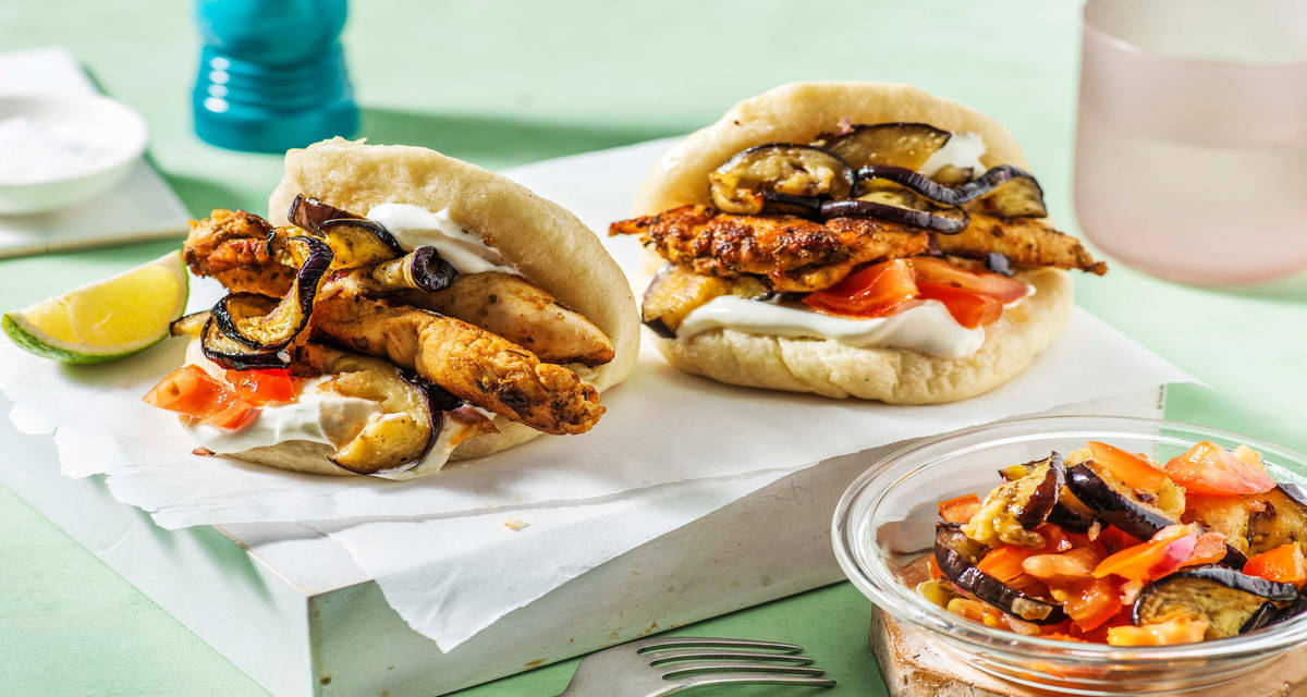 Gyros de poulet au paprika fumé servi dans des pains Bao avec du yaourt aux herbes, des aubergines rôties et des tomates