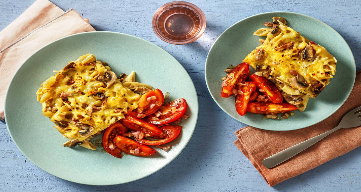 Gratin de pâtes aux lardons, champignons & oignons avec du râpé de raclette et une salade de tomate