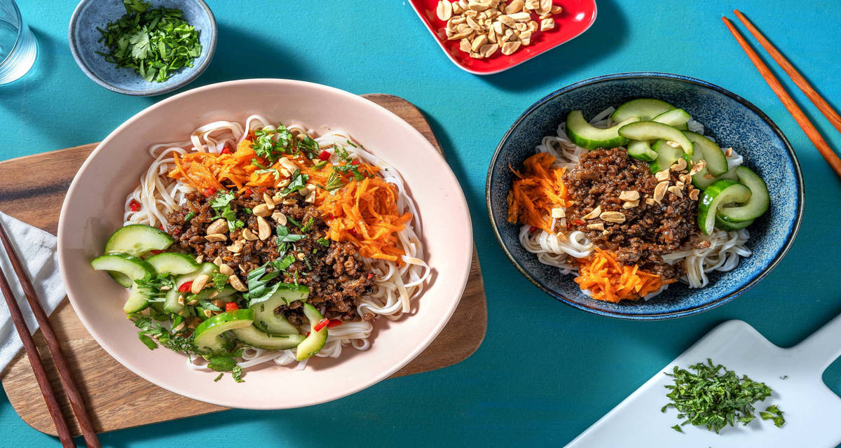 Bò bún vietnamien au bœuf sauté servi avec du concombre, des carottes râpées et des cacahuètes