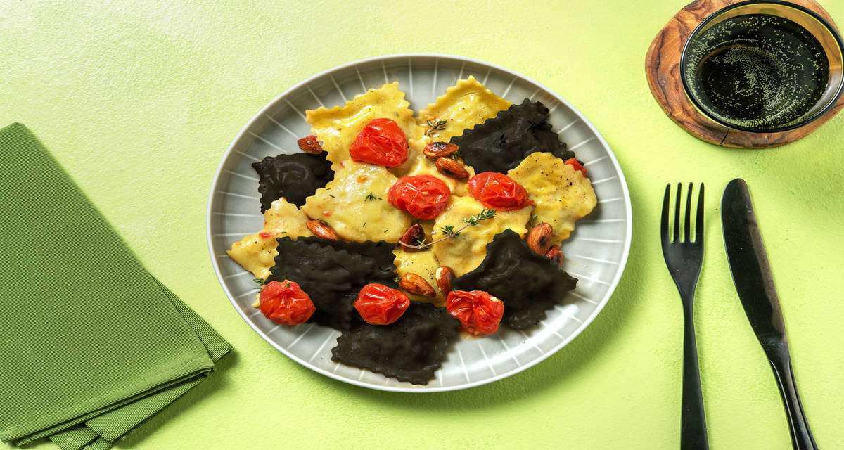 Ravioli al nero di seppia ripieni di nasello con pomodorini caramellati, mandorle e timo