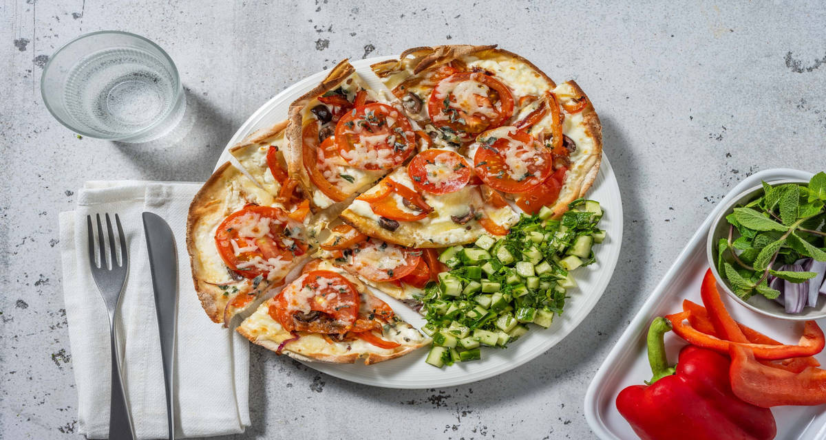 Pizza sur pain plat à la grecque et salade de concombre garnie de fromage grec et d'olives