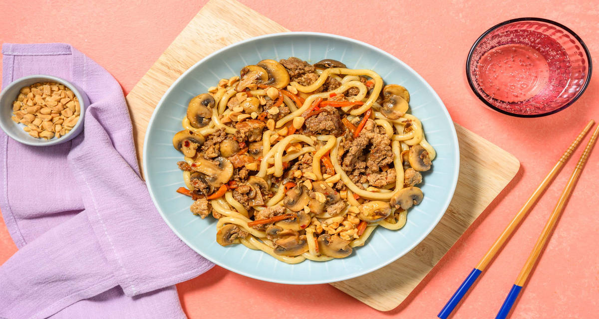 Udon spicy saltati alla salsiccia e funghi con salsa di soia, peperoncino e arachidi