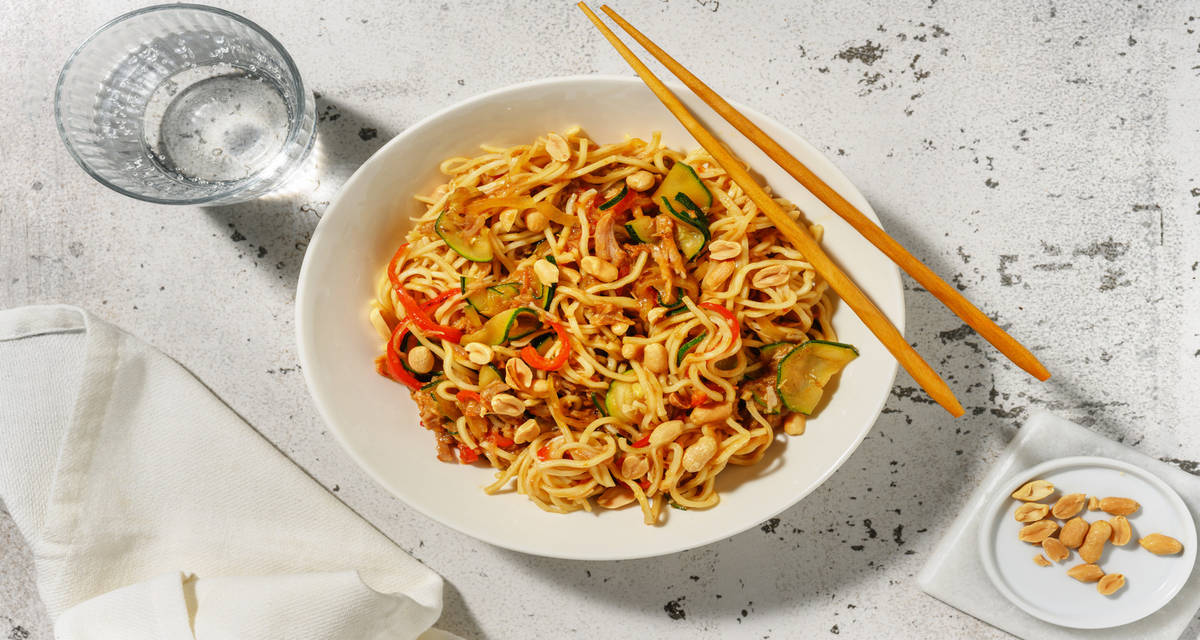 Wok de nouilles complètes au porc effiloché garnies de légumes d'été sautés & cacahuètes