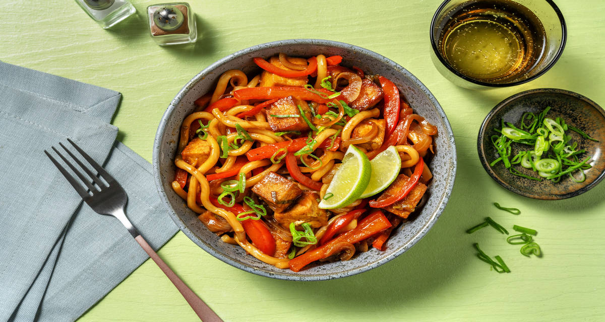 Fideos udon con tofu salteado acompañado de verduras, ajo tierno y lima