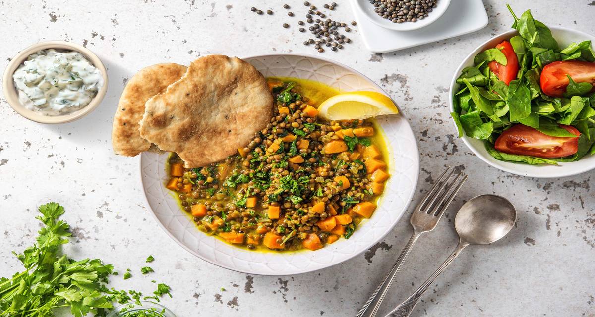 Mijoté de lentilles à l'indienne et pain naan servis avec une salade d’épinards et une sauce au yaourt