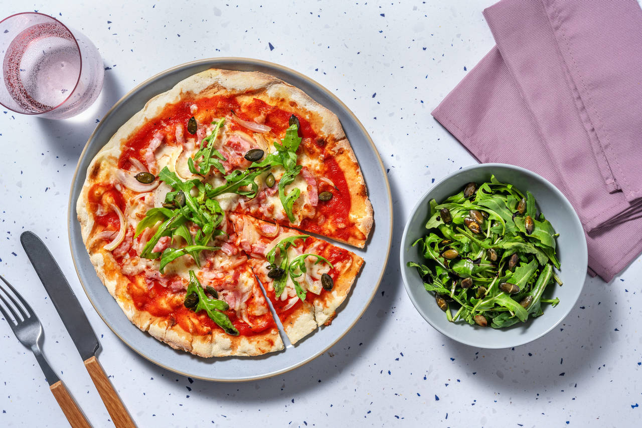 Pizza de bacon y cebolla con rúcula y semillas de calabaza tostadas