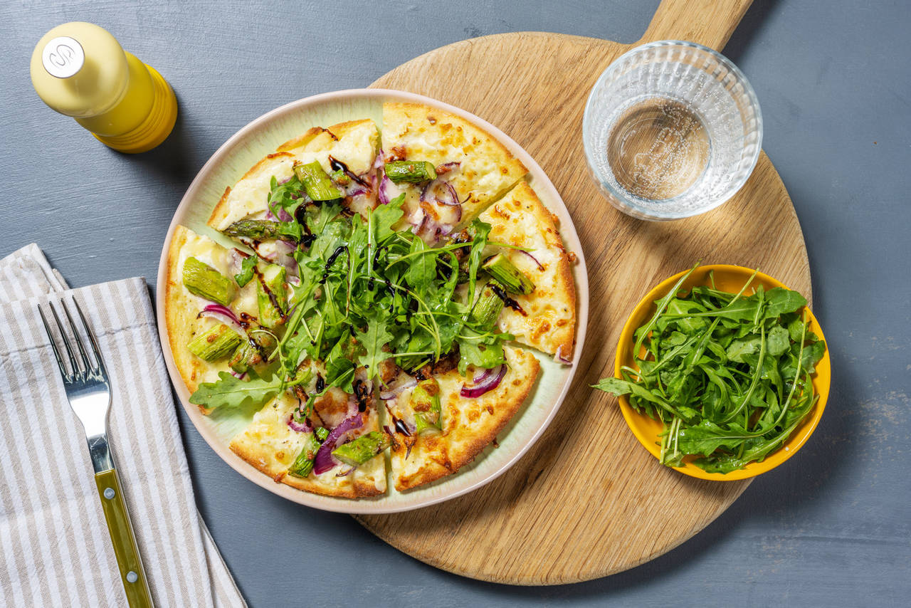 Pizza con espárragos y cebolla acompañada de crema de vinagre balsámico y rúcula