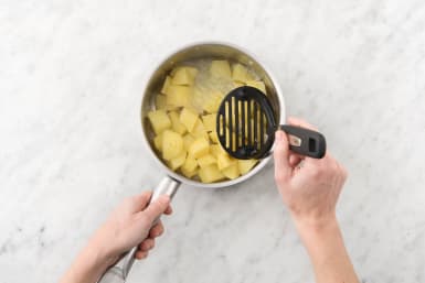Stamp de ui en aardappelen met een aardappelstamper tot een puree