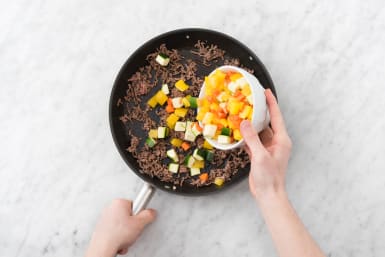 Verhit de roomboter in een wok of hapjespan met deksel. Bak daarin het rundergehakt met de knoflook en Italiaanse groentemix in 3 minuten