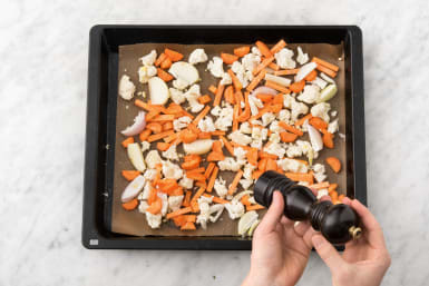 Verdeel de aardappelen, knoflook, ui, peen en de mix van bloemkool en bataat over een bakplaat met bakpapier.