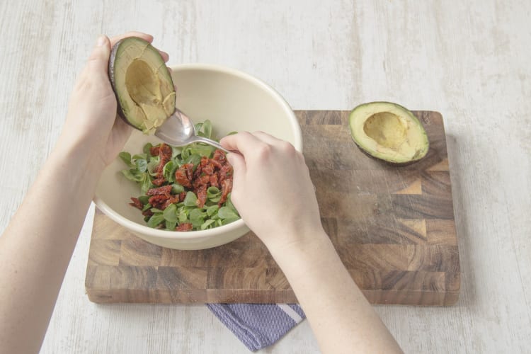 Meng de veldsla, semi-zongedroogde tomaten, avocado en tijm in een saladekom.