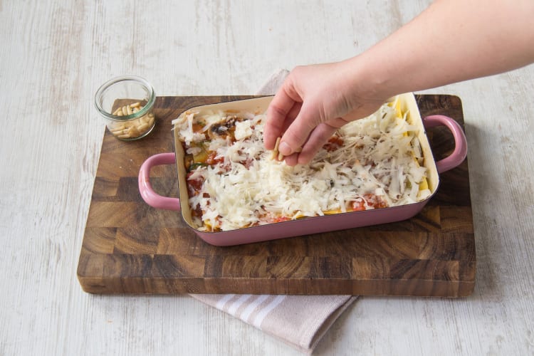 Eindig de lasagne met een laagje saus, provolone, pijnboompitten en versgemalen peper