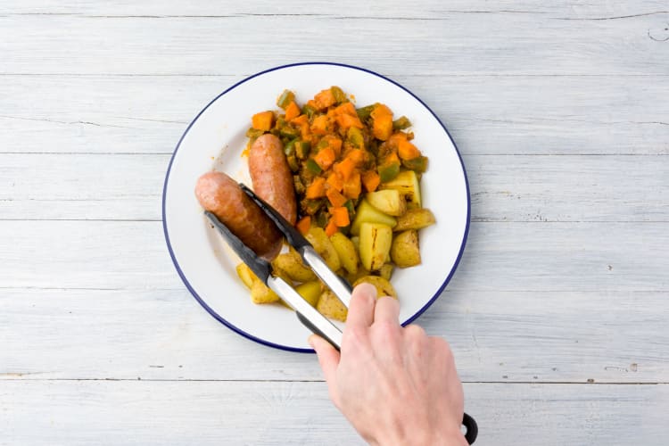 Verdeel de wildzwijnworstjes, de ratatouille en de krieltjes over de borden.