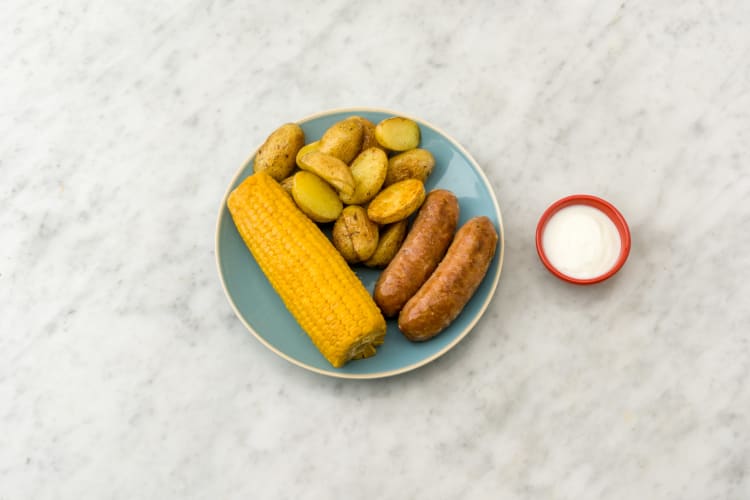 Verdeel de kipsaucijsjes, maïskolf en krieltjes over de borden.