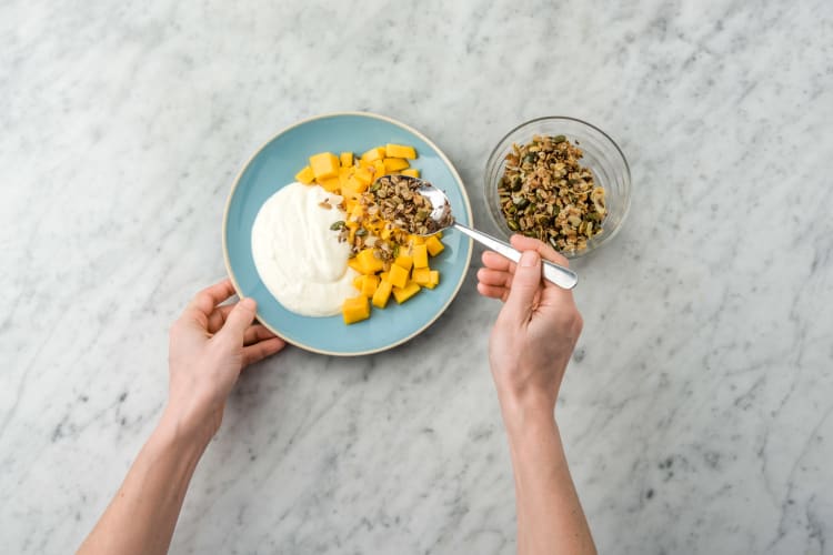 Laat de granola afkoelen, verbrokkel het in kleine stukjes en bestrooi hiermee de mango.