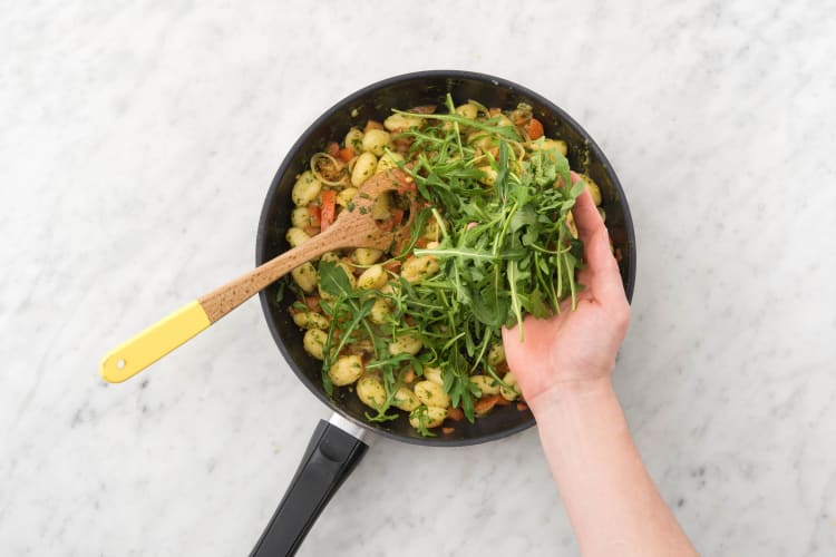 Voeg de gnocchi, tomaat, pesto en de helft van de rucola toe en bak 3 minuten op hoog vuur. Breng op smaak met peper en zout