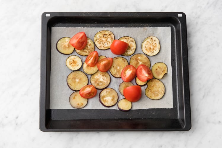 Leg de aubergine en tomaat op een bakplaat