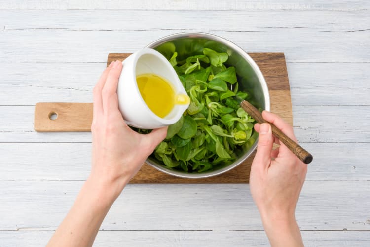 Meng de dressing met de veldsla in een saladekom