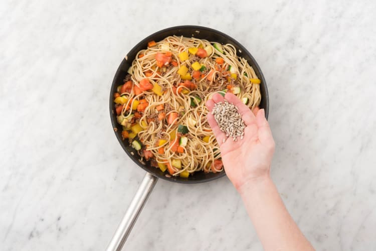 Voeg de spaghetti en de helft van de zonnebloempitten toe aan de saus en verhit nog 1 minuut