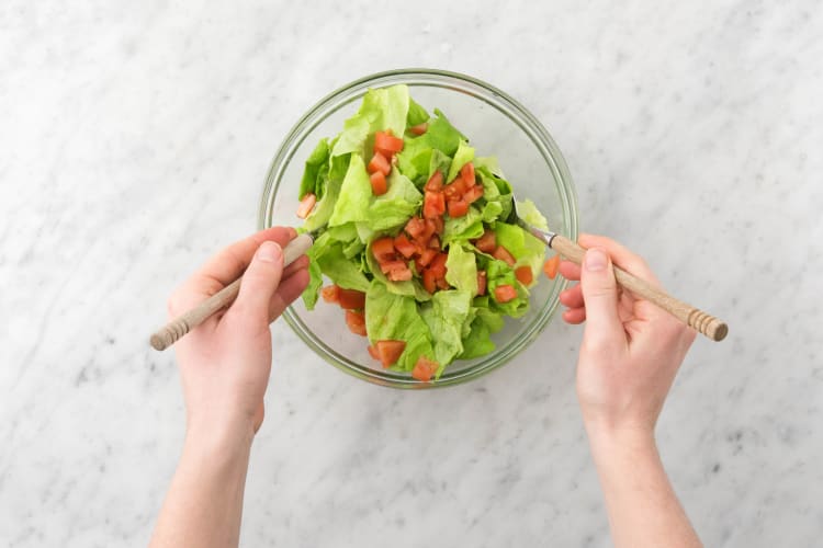 Meng de rest van de botersla en kleingesneden tomaat met de extra vierge olijfolie en witte wijnazijn in een saladekom